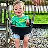 Harper is registered to the contest to win money with this photo: toddler, child, baby, smiling, playground, swing, outdoor, sunset, backyard, grass, trees, basketball_hoop, fence, playground_surface, wood_chips, green_shirt, shorts, barefoot, portrait, happy