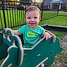 baby, child, toddler, smiling, outdoor, playground, rocking_toy, train, toy, green_shirt, little_brother, face, portrait, lawn, fence, suburban, house, grass, evening_light, playtime