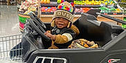Zymir is registered to the contest to win money with this photo: toddler, child, shopping_cart, grocery_store, hat, colorful, flames, black, produce, fruit, vegetables, smile, clothing, toy_car, indoor, aisle, shopping, person, cute, fun