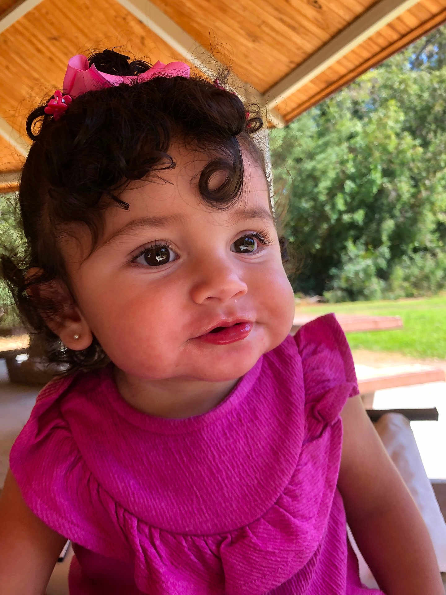 Liliana is registered to the contest to win money with this photo: toddler, child, curly_hair, pink_dress, outdoor, portrait, cute, smiling, earrings, ribbon, daylight, nature, pavilion, bench, greenery, face, person, happy, young_child, closeup