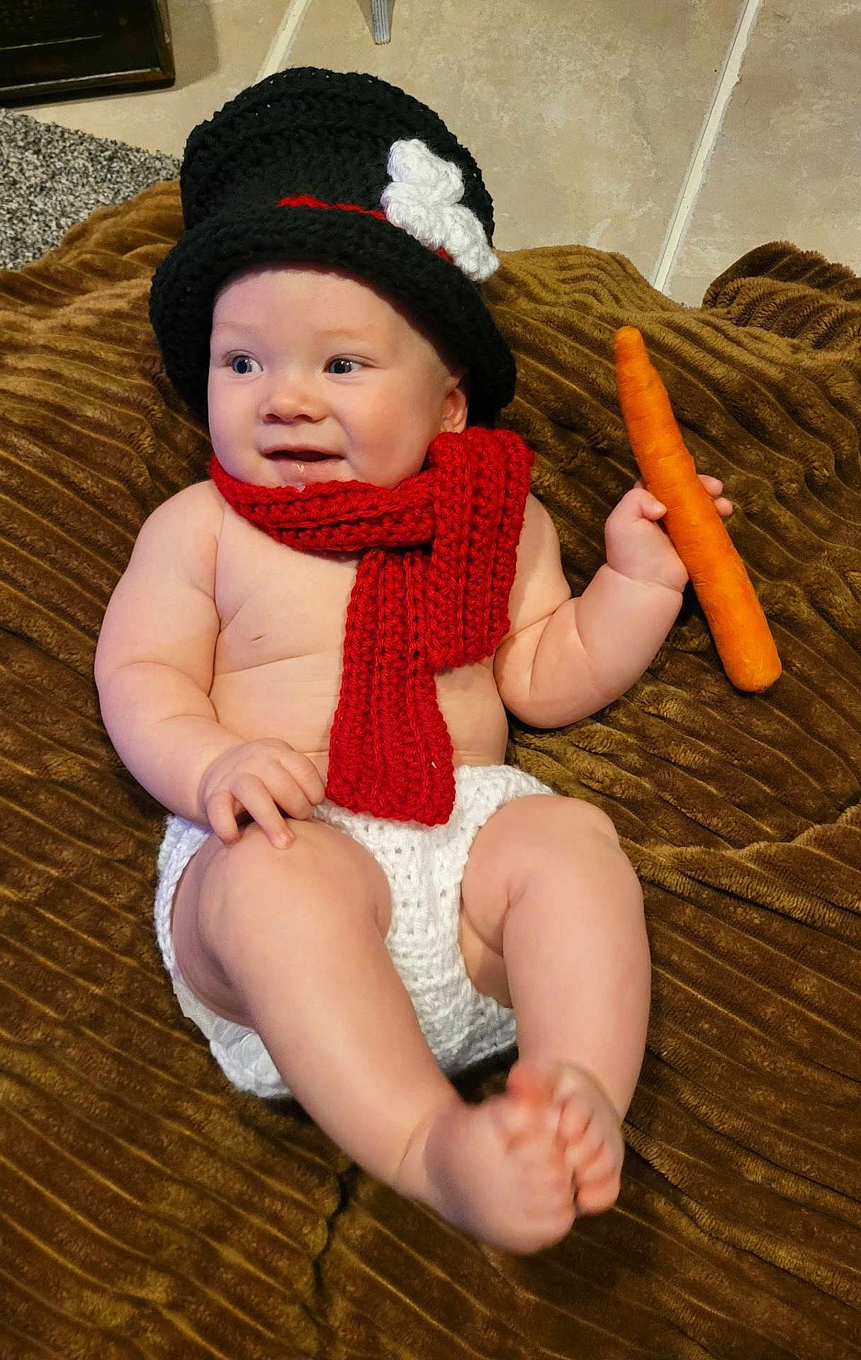 Kingston is registered to the contest to win money with this photo: baby, child, infant, hat, scarf, carrot, blanket, knitwear, cute, smiling, sitting, indoor, floor, clothing, person, portrait, toddler, skin, hand, foot