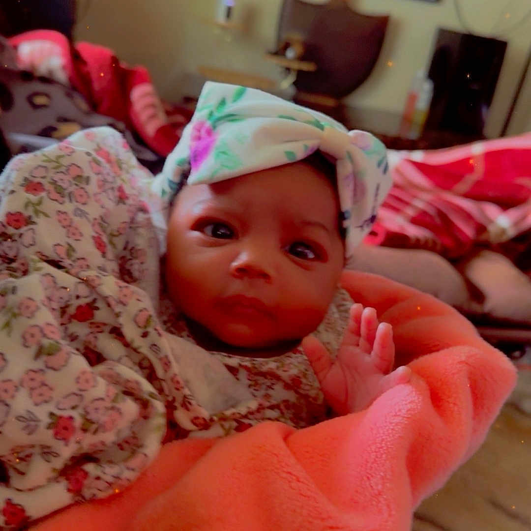 Amina joined the competition — help win amazing prizes! baby, infant, blanket, headband, floral, indoors, person, face, cute, clothing, cozy, child, portrait, looking, hand, fabric, warm, room, decor, soft