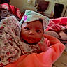 Amina is registered to the contest to win money with this photo: baby, infant, blanket, headwrap, floral, clothing, face, person, indoor, living_room, furniture, couch, table, decor, soft_texture, cute, curious, child, portrait, warm
