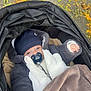 baby, stroller, pacifier, hat, jacket, blanket, autumn, leaves, outdoor, child, cute, warm_clothing, infant, cozy, fall, pavement, person, baby_clothes, relaxing, wrapped