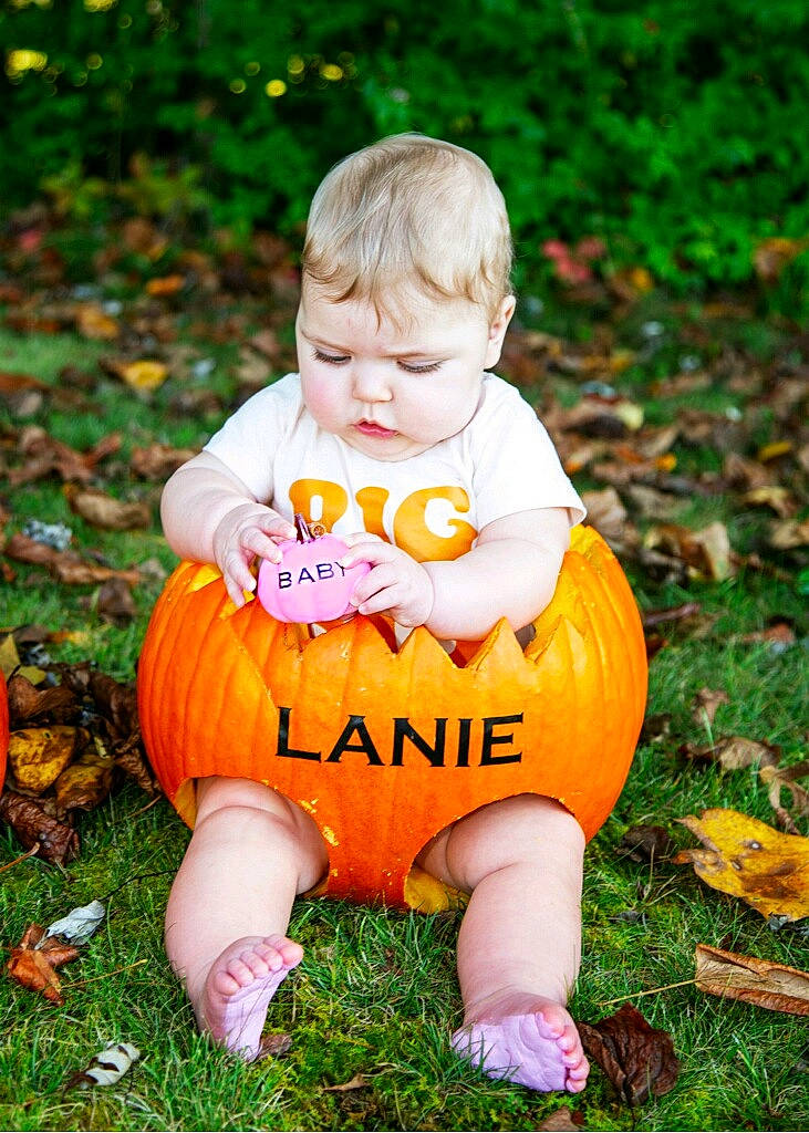 Delanie is registered to the contest to win money with this photo: baby_toddler_clothing, calabaza, child, dress, footwear, grass, happy, head, lawn, leg, orange, people_in_nature, person, plant, pumpkin, shoe, smile, toddler, tree, vegetable