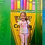 child, girl, smiling, standing, crayola, crayons, colorful, tshirt, leggings, purple_shoes, braid, indoor, poster, background, playful, happy, toy, art, yellow, green