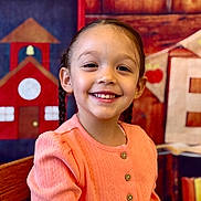 Sabrina is registered to the contest to win money with this photo: child, girl, smiling, braided_hair, peach_sweater, portrait, indoor, school_theme, colorful_background, wooden_chair, happy, face, cute, young, buttoned_sweater, closeup, warm_colors, education, decor, person