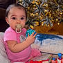 baby, blue_ball, book, child, christmas_tree, couch, cute, decorations, festive, floor, holiday, indoor, lights, ornaments, pacifier, person, pillow, pink_clothing, portrait, toys