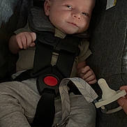 Beckett is registered to the contest to win money with this photo: baby, infant, car_seat, safety_harness, pacifier, hand, clothing, foot, grey_pants, indoor, child, seat_belt, resting, cute, newborn, person, comfort, straps, fabric, closeup