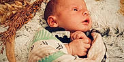Beckett is registered to the contest to win money with this photo: baby, newborn, blanket, swaddled, infant, face, hand, lying_down, looking_up, fluffy_rug, dried_plants, natural_decor, cozy, soft_texture, portrait, cute, peaceful, child, indoors, warm_colors