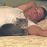 man, cat, bed, white_shirt, tabby_cat, relaxing, indoor, pillow, blanket, bedroom, resting, pet, feline, human, comfort, cozy, lying_down, arm, fur, sleepy