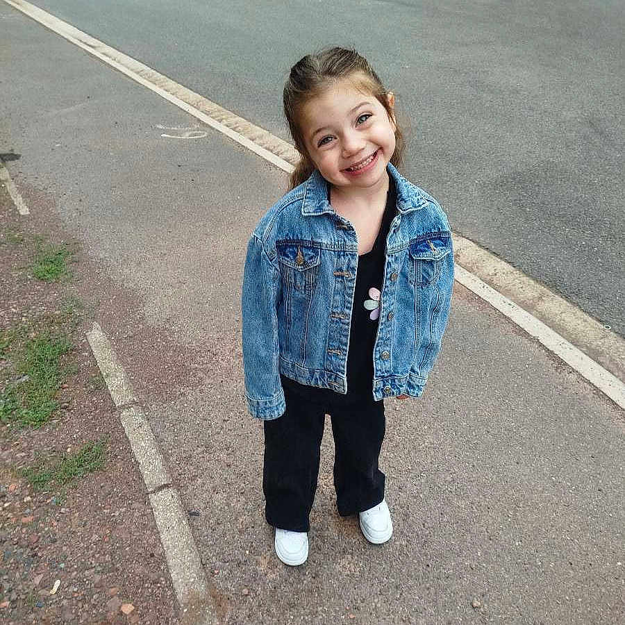 Juditte a rejoint le concours — aidez-le/la à gagner de superbes lots ! black_pants, car, casual_clothing, child, curly_hair, daylight, denim_jacket, girl, happy, nature, outdoor, pavement, person, posing, road, sidewalk, smiling, street, urban, white_shoes