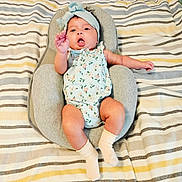 Samantha is registered to the contest to win money with this photo: baby, infant, headband, romper, socks, baby_seat, striped_blanket, cute, child, lying_down, raised_hand, expression, indoor, soft_furniture, patterned_clothing, newborn, comfortable, skin, person, adorable