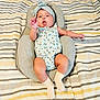 baby, infant, headband, romper, socks, baby_seat, striped_blanket, cute, child, lying_down, raised_hand, expression, indoor, soft_furniture, patterned_clothing, newborn, comfortable, skin, person, adorable