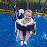 baby, child, swing, playground, smiling, happy, blue_surface, blanket, stroller, outdoor, trees, fence, person, feet, socks, seat, metal_chains, sunlight, greenery, fun