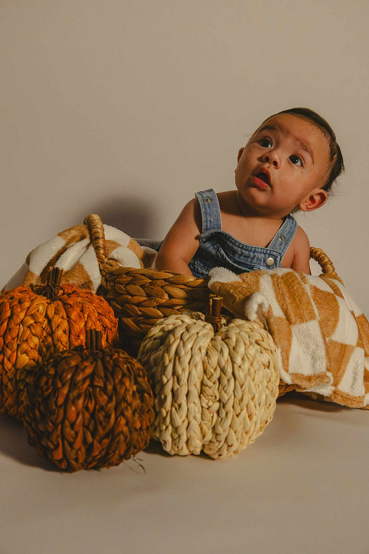 Alessandro is registered to the contest to win money with this photo: baby, child, basket, denim_overalls, decorative_pumpkins, woven, blanket, curious, indoor, studio, portrait, fall_decor, cozy, neutral_background, cute, sitting, infant, expression, textile, holiday