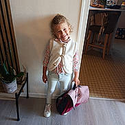 Lalie participe au concours pour gagner de l'argent avec cette photo : child, smile, curly_hair, indoor, wall, bag, white_vest, floral_shirt, light_jeans, white_sneakers, plant, chair, kitchen, floor, window, table, person, happy, standing, home