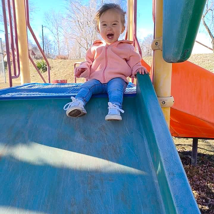 Timber is registered to the contest to win money with this photo: baby_toddler_clothing, blue, child, chute, city, electric_blue, fun, grass, leisure, outdoor_play_equipment, outdoor_recreation, person, play, playground, playground_slide, recreation, sitting, sky, toddler, tree