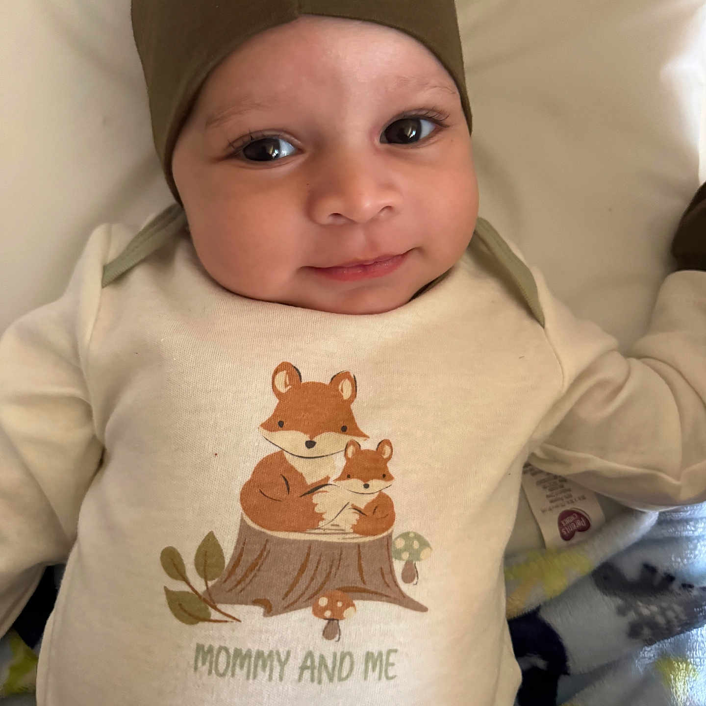 Xaidyn is registered to the contest to win money with this photo: adorable, apparel, baby, blanket, child, clothing, cozy, cute, face, fox_illustration, hat, headwear, infant, lying_down, portrait, shirt, smile, soft_texture, toddler, warm_colors