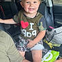 child, toddler, smiling, car_interior, seat, tshirt, camo_clothing, handbag, baby_wipes, adult_arm, window, trees, seatbelt, shorts, person, happy, interior, travel, family, casual