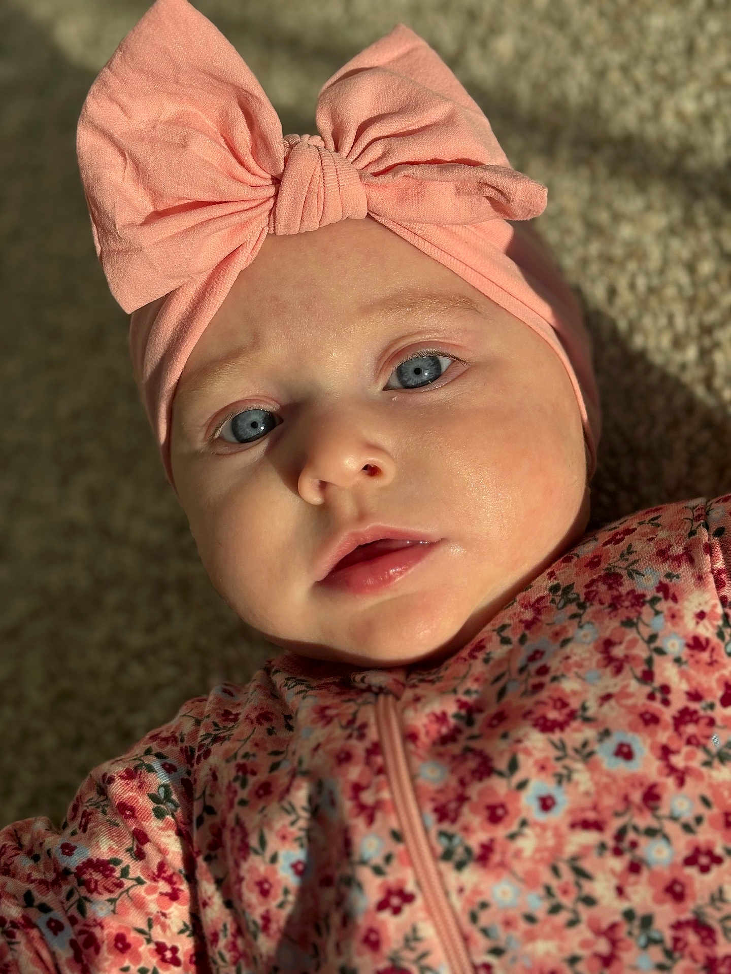 Lainey is registered to the contest to win money with this photo: baby, blue_eyes, bow, child, close_up, cute, face, floral_pattern, headband, infant, indoors, light, looking_at_camera, person, pink, portrait, skin, soft_texture, toddler, warm_light