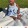 baby, barefoot, blanket, blue_clothing, bow, child, facial_expression, grass, headband, outdoor, park, portrait, screenshot, sitting, smiling, social_media, striped_dress, sunlight, toddler, white_clothing