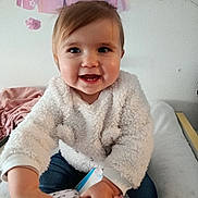 Anais participe au concours pour gagner de l'argent avec cette photo : toddler, child, smiling, indoor, white_sweater, toy, box, curly_hair, happy, person, baby, cute, playful, jeans, face, hands, butterfly, wall_decor, soft_lighting, cozy