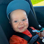 Noah joined the competition — help win amazing prizes! baby, child, smile, cap, car_seat, safety_harness, orange_shirt, blue_cap, happy, face, person, infant, seatbelt, cute, indoors, car, seat, young_child, portrait, bright
