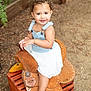 Zaya is registered to the contest to win money with this photo: toddler, child, smiling, curly_hair, denim_overall, white_skirt, saddle, wooden_crate, outdoor, dirt_ground, fence, nature, happy, portrait, barefoot, person, playful, sunlight, young_child, cute