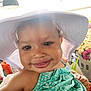 baby, child, hat, smile, face, flower_market, bouquet, flowers, sunlight, green_dress, skin, cheeks, close_up, baby_clothing, happy, person, portrait, indoor, headwear, cute