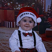 Sandro participe au concours pour gagner de l'argent avec cette photo : baby, child, santa_hat, christmas, holiday, festive, lights, plaid, bow_tie, suspenders, white_shirt, smiling, happy, indoors, decorations, present, floor, cute, portrait, celebration
