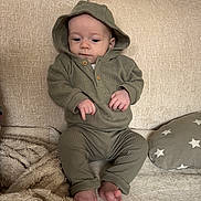 Onnie-Clay is registered to the contest to win money with this photo: baby, child, hoodie, green_clothing, couch, blanket, pillow, indoor, infant, sitting, feet, hands, face, expression, cozy, fabric, soft_texture, home, casual, portrait