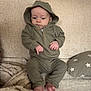baby, child, hoodie, green_clothing, couch, blanket, pillow, indoor, infant, sitting, feet, hands, face, expression, cozy, fabric, soft_texture, home, casual, portrait