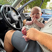 Onnie-Clay is registered to the contest to win money with this photo: adult, baby, car_interior, casual, cute, daylight, door, feet, fingers, hand, happy, infant, nature, person, seat, shorts, smile, steering_wheel, trees, window