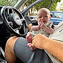 adult, baby, car_interior, casual, cute, daylight, door, feet, fingers, hand, happy, infant, nature, person, seat, shorts, smile, steering_wheel, trees, window