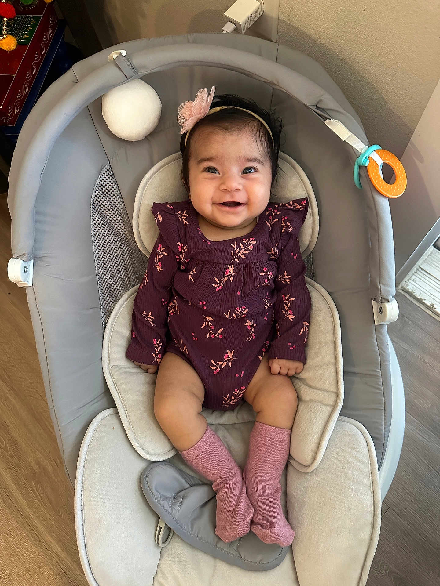 Harnoor joined the competition — help win amazing prizes! baby, infant, smiling_baby, onesie, headband, pink_socks, baby_seat, bouncer, toy_ring, soft_ball, chubby_cheeks, dark_hair, indoor, wood_floor, cozy, portrait, happy, hands, legs, cute
