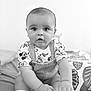 baby, bed, black_and_white, blanket, child, curious, cute, expression, face, feet, hands, indoors, infant, mickey_mouse, overalls, pillow, portrait, shirt, sitting, young