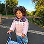Lou a rejoint le concours — aidez-le/la à gagner de superbes lots ! child, curly_hair, jacket, toy_stroller, jeans, outdoor, smiling, blue_sky, greenery, pavement, bow, happy, play, person, daylight, casual_clothing, walking, young, cute, nature