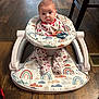 baby, infant, baby_walker, rainbow_pattern, footwear, wooden_floor, indoor, clothing, face, person, sitting, toy, chair_leg, vent, cute, child, plush, patterned_clothing, expression, flooring