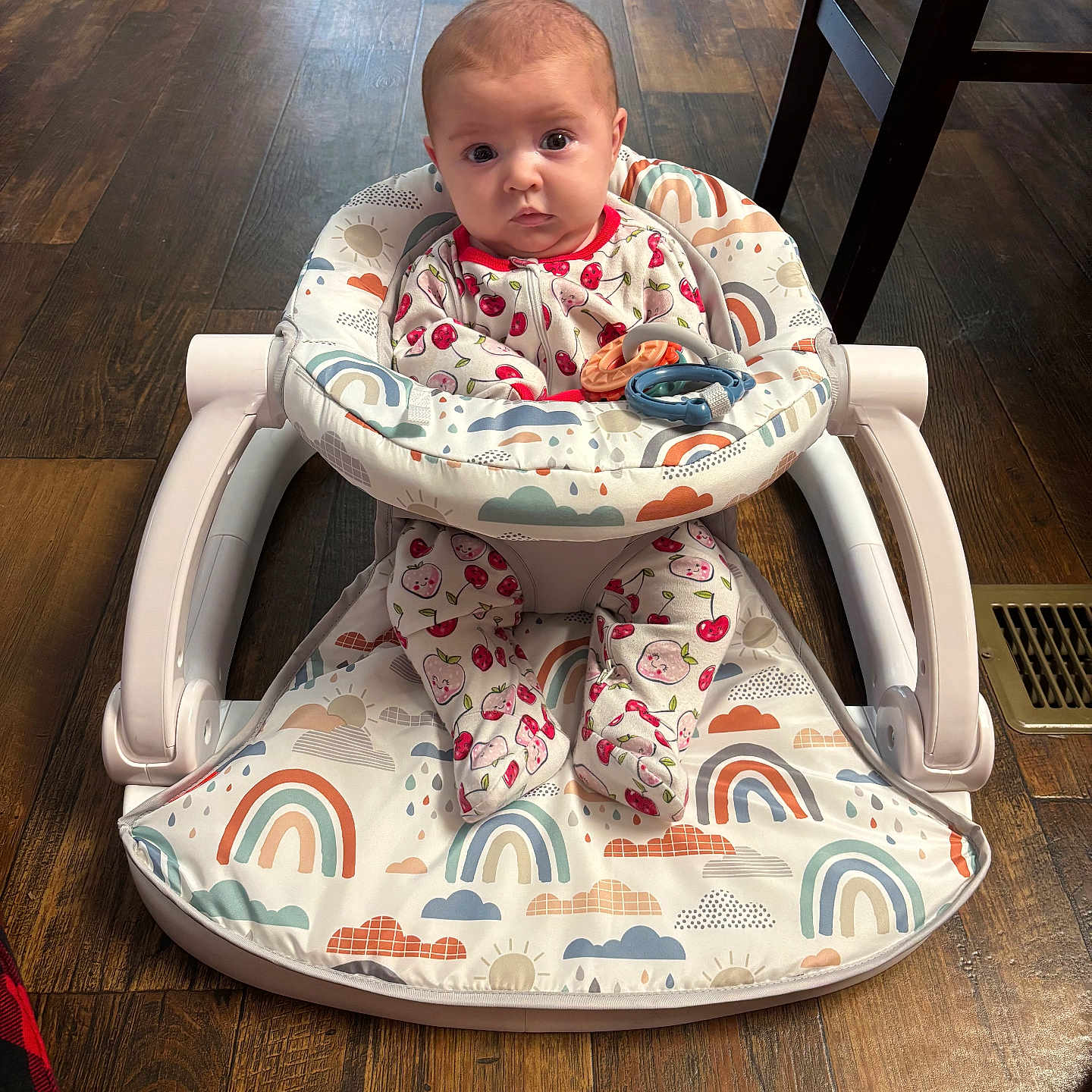 Sonney is registered to the contest to win money with this photo: baby, baby_walker, chair_leg, child, clothing, cute, expression, face, flooring, footwear, indoor, infant, patterned_clothing, person, plush, rainbow_pattern, sitting, toy, vent, wooden_floor
