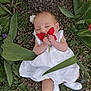 baby, infant, child, white_dress, red_flower, holding_flower, leaves, grass, tree_bark, outdoor, nature, sleeping, tiny_hands, socks, portrait, top_down_view, cute, newborn, blossom, green_foliage