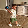 Milan is registered to the contest to win money with this photo: toddler, child, indoor, ball, throwing, wooden_floor, shorts, shirt, animal_print, sneakers, furniture, cabinet, living_room, person, floor, concentration, walking, toy, home, young_child