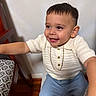 Milan joined the competition — help win amazing prizes! toddler, child, smiling, indoor, white_shirt, blue_shorts, chair, wooden_floor, gold_chain, happy, cute, person, short_hair, patterned_cushion, sitting, reaching_out, portrait, fashion, casual, home