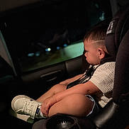 Milan is registered to the contest to win money with this photo: child, toddler, car_seat, side_view, night, window, shoes, shorts, haircut, seatbelt, car_interior, pensive, casual_clothing, young_child, sitting, closeup, indoors, safety, quiet, portrait