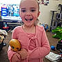 child, smiling, pink_clothing, toy, living_room, television, carpet, furniture, cat_tree, ball, photo_wall, window, happy, indoor, person, playful, home, young_child, cute, holding