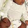 baby, infant, child, onesie, baby_seat, patterned_fabric, geometric_pattern, sitting, curious_expression, dark_skin, short_hair, indoor, clothing, hand, foot, legs, face, person, comfortable, seatbelt