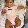 baby, infant, onesie, pink_clothing, smile, face, child, butterfly_pattern, blanket, laying_down, happy, cute, skin, person, indoors, toy, hand, feet, curly_hair, playpen