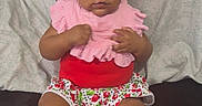 Brielle is registered to the contest to win money with this photo: baby, child, infant, headband, flower, pink_clothing, red_clothing, shorts, patterned_clothing, pacifier, sitting, couch, pillows, indoor, portrait, cute, feet, hands, looking_at_camera, person