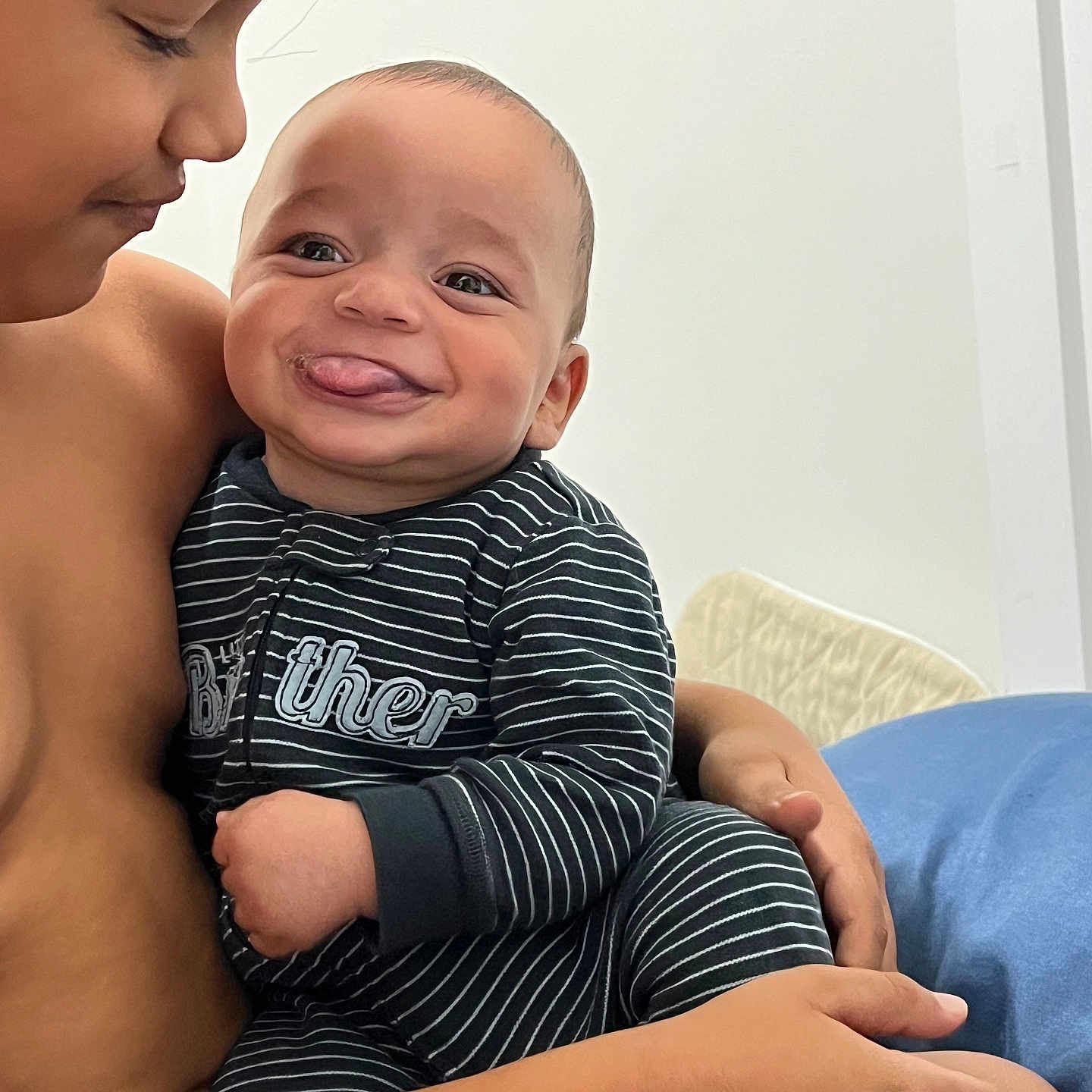 Nolan is registered to the contest to win money with this photo: baby, child, siblings, smile, tongue_out, striped_clothing, indoor, hug, love, happy, portrait, person, skin, face, arm, hand, bed, blanket, candid, cute
