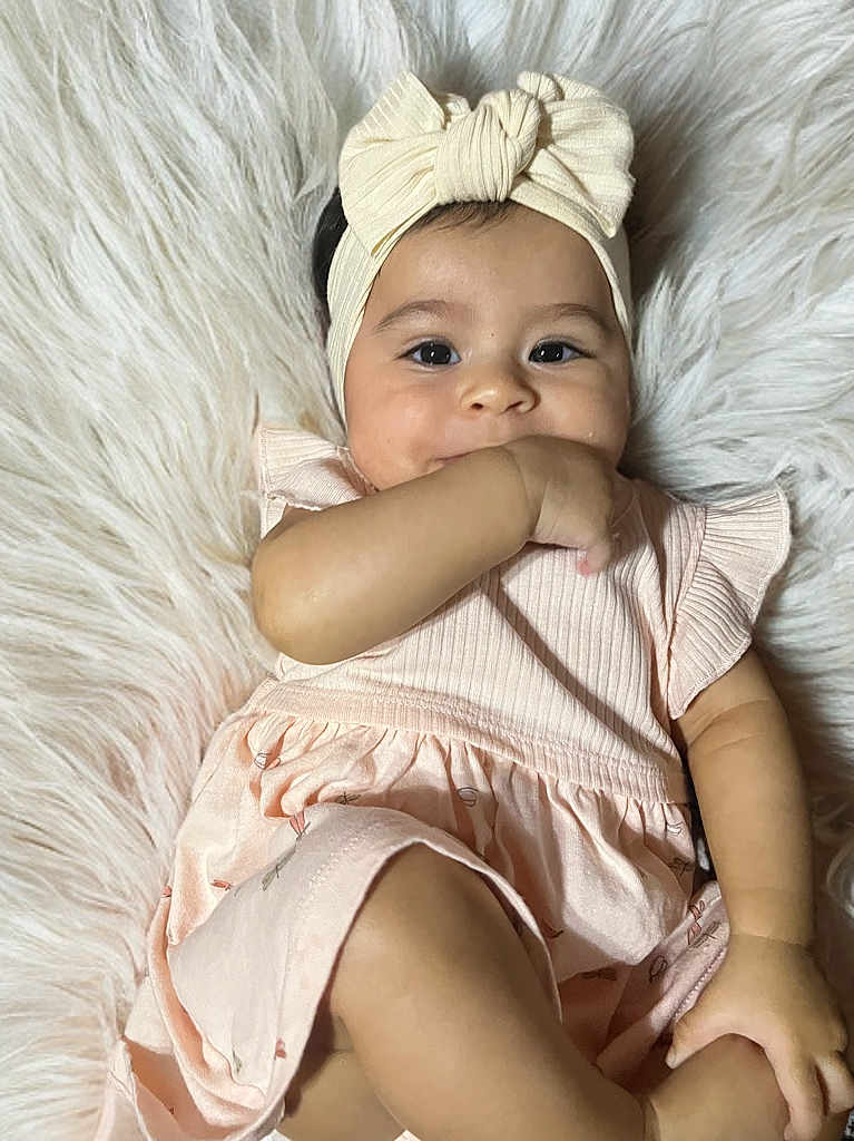 Eilany is registered to the contest to win money with this photo: baby, girl, infant, headband, bow, pink_dress, fluffy_rug, hand_in_mouth, cute, smiling, portrait, child, soft_texture, indoor, close_up, skin, face, eyes, young, comfortable